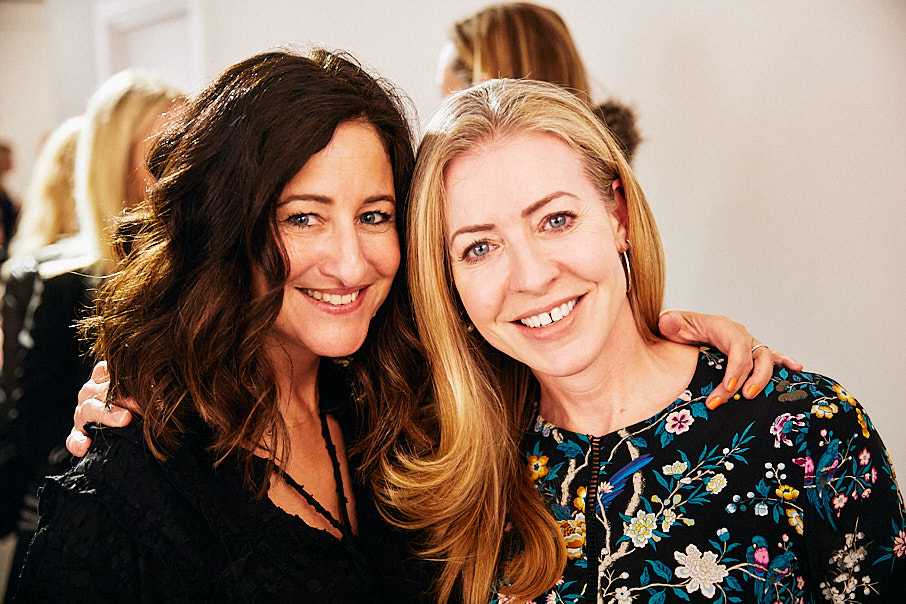 Two women arm in arm smiling at a beauty event
