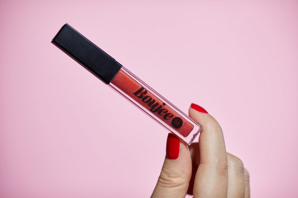 Lip gloss in hand against pink background