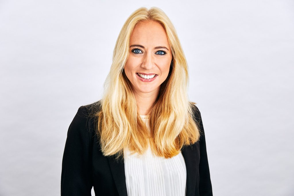 Business headshot of women in black jacket with long blonde hair against a white background