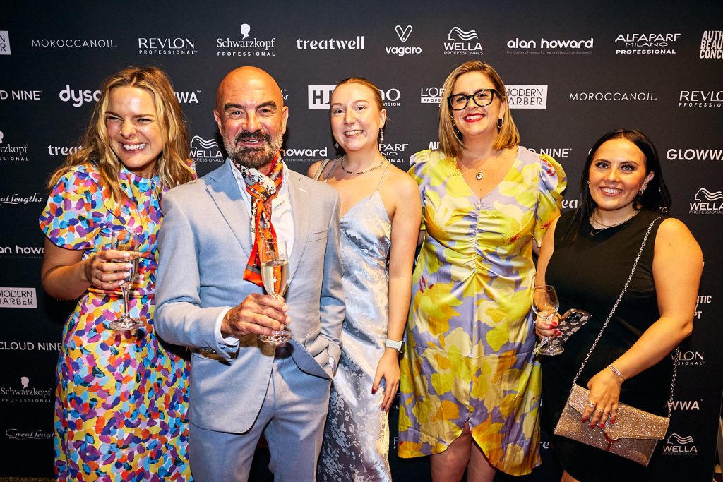 Five adult guests of the British Hairdressing Business Awards photographed in front of a step and repeat board