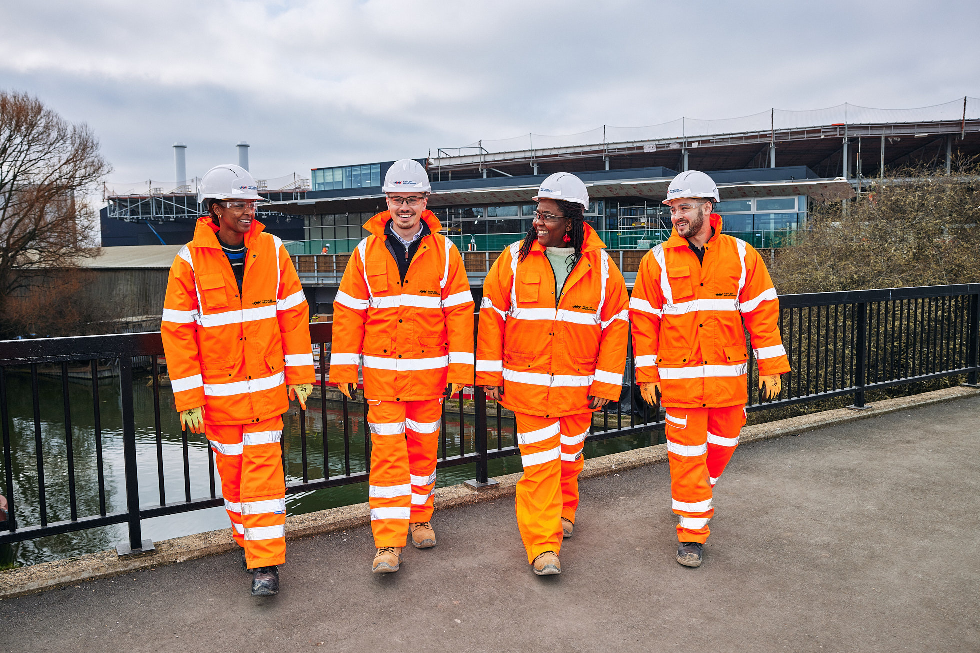 Four people where hi-viz trousers, jackets and hard hats, walking in a line on a construction site