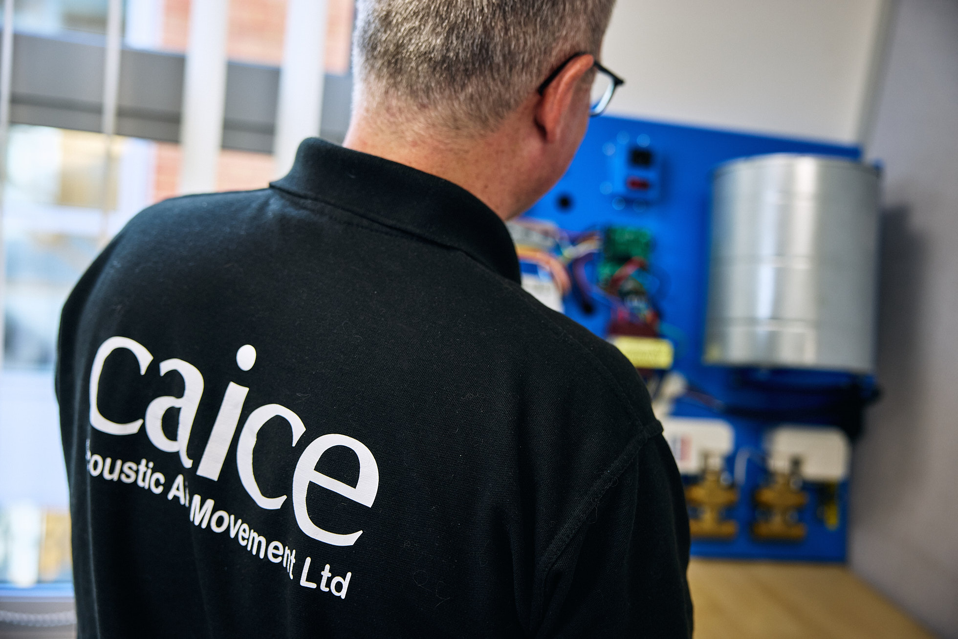 Man in an office wearing a branded polo shirt photographed from behind