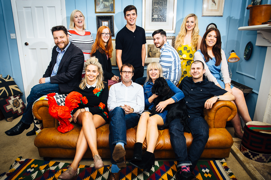 A group of colleagues sat around a brown leather sofa, laughing and smiling.