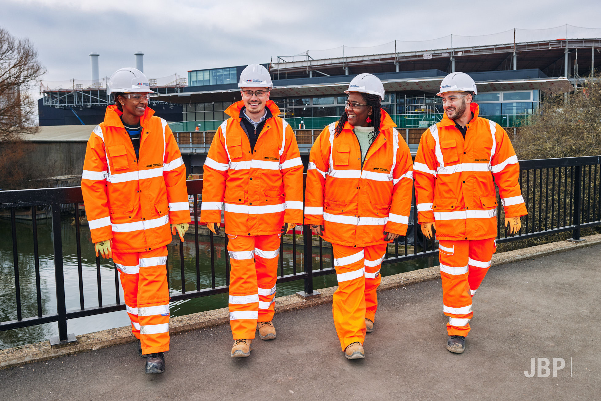 Four colleagues in high visibility clothing and hard hats walking towards the camera against the backdrop of a business site.