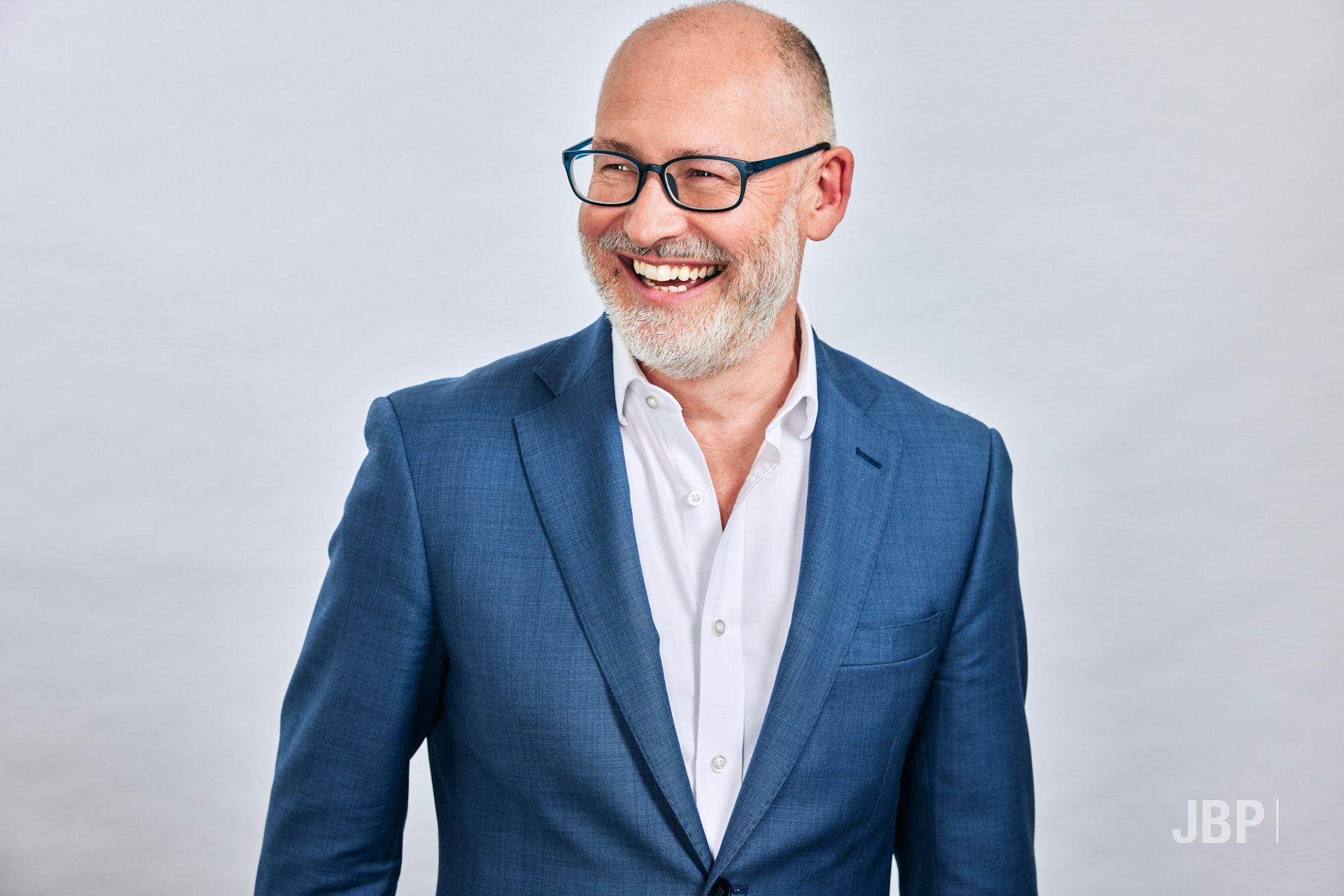 Professional portrait of a man looking off camera in a white shirt and blue blazer against a light grey background.