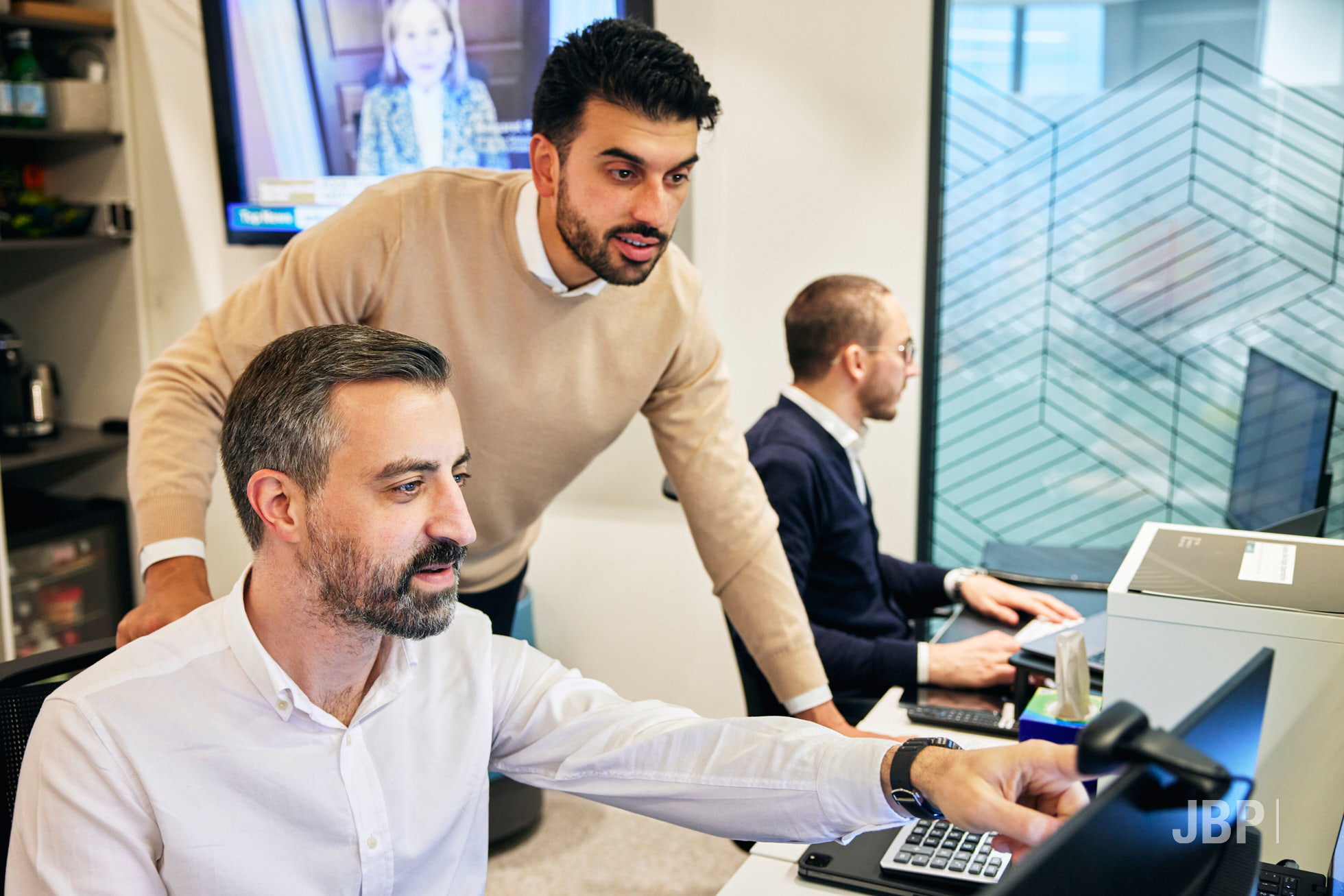 Corporate lifestyle photography showing three men, two looking at a computer screen and one in the background working.
