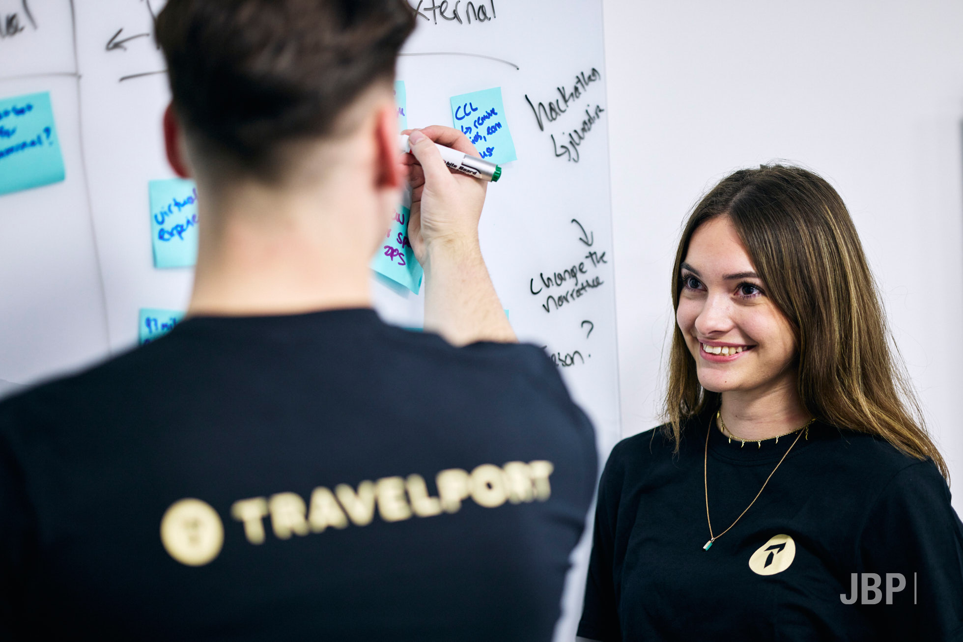 Corporate lifestyle photography showing a woman smiling at a colleague who is in the foreground writing notes on a white board.