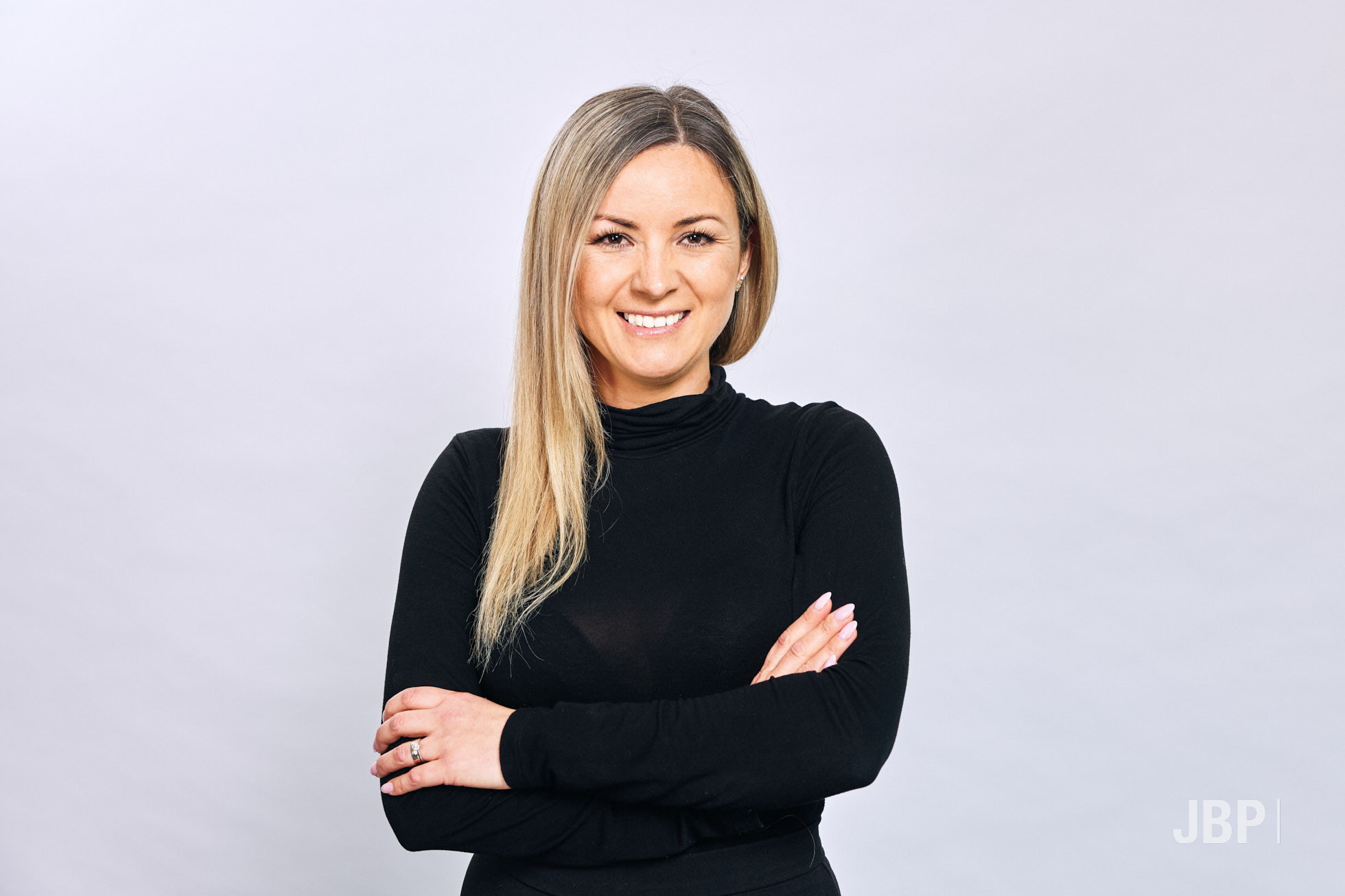 Professional headshot of a young woman with long blonde hair wearing a black top with her arms folded